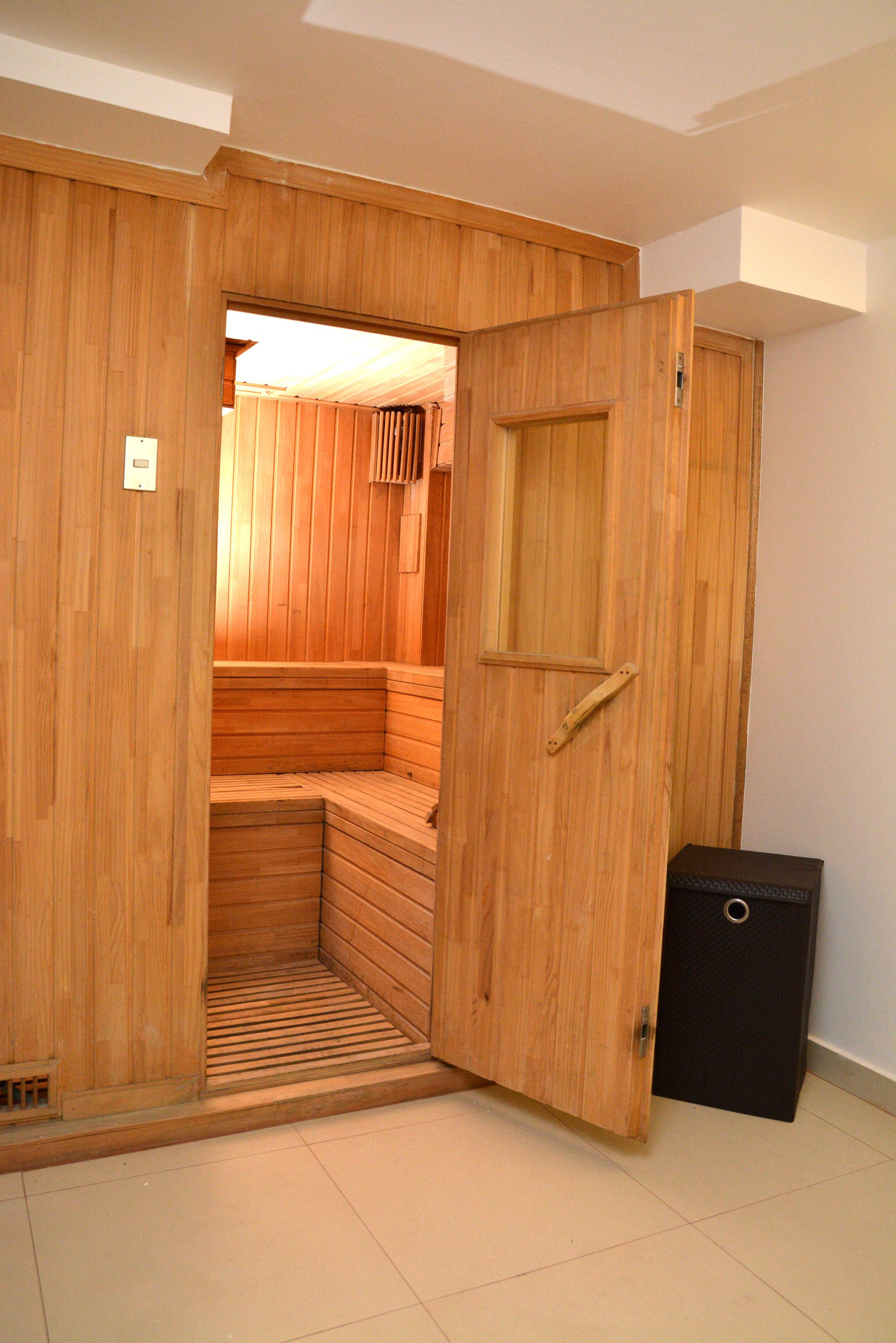 A wooden sauna room with a bench, a door, and a small black cabinet.