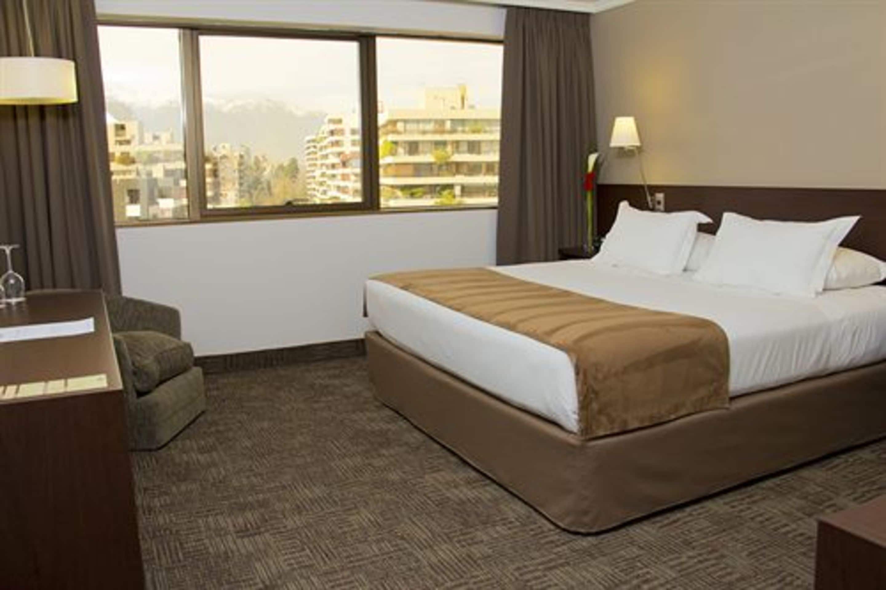 Een hotelkamer met een groot bed, een bureau, een stoel en uitzicht op gebouwen.
