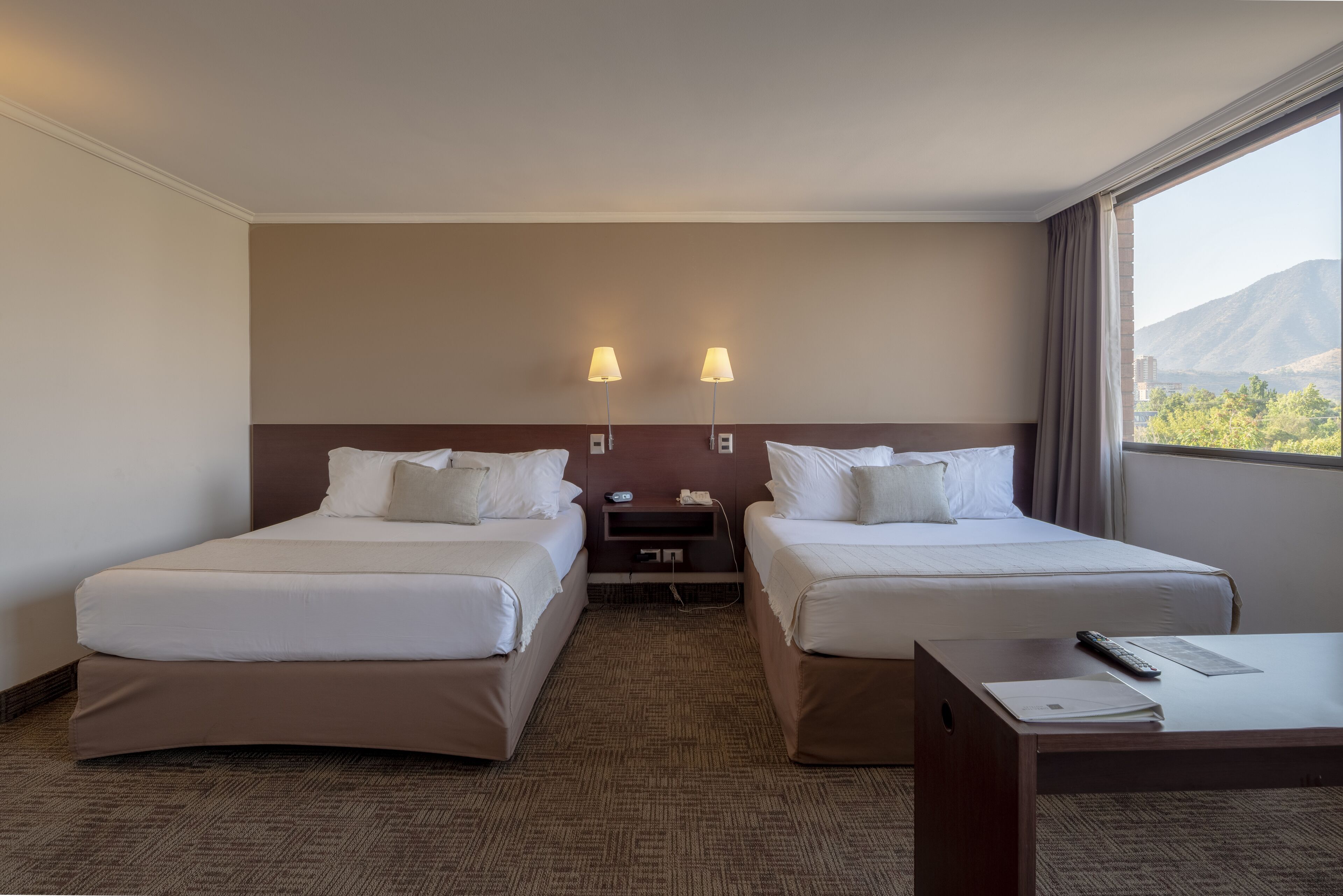 A hotel room with two beds, a desk, and a nightstand with lamps.