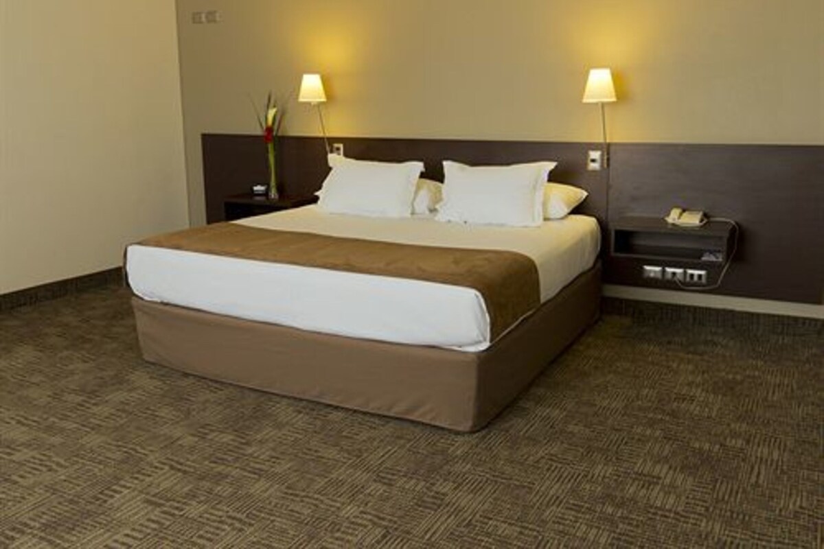 A hotel room with a large bed, two bedside lamps, a nightstand, and a dresser.