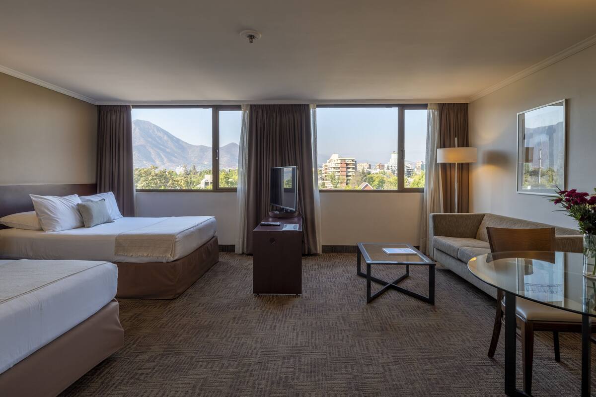 Ein Hotelzimmer mit zwei Betten, einem Sofa, einem Fernseher und einem Tisch.