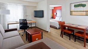 Habitación de hotel con cama, escritorio con silla, televisión y mesa de comedor con sillas.