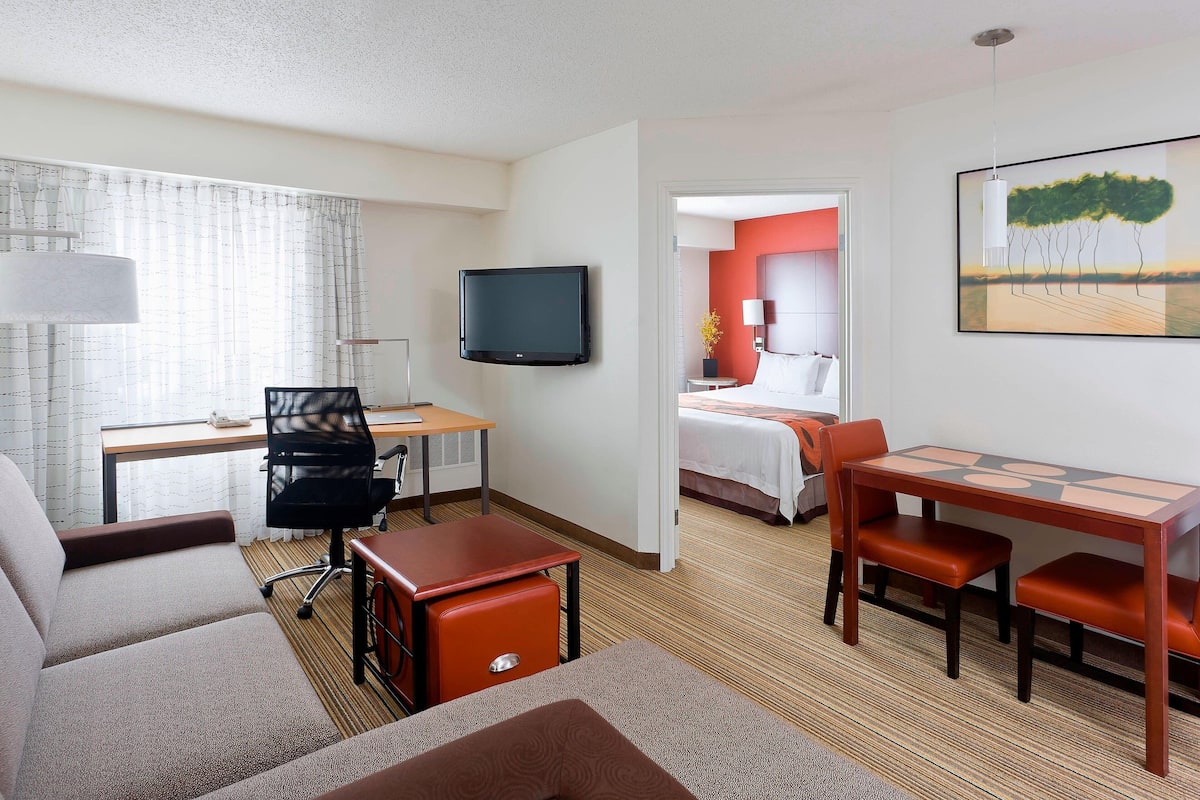 A hotel room with a bed, a desk with a chair, a TV, and a dining table with chairs.