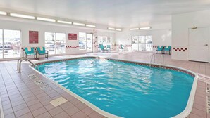 Una piscina interior con agua cristalina, suelo de baldosas y varias sillas alrededor de la zona de la piscina.