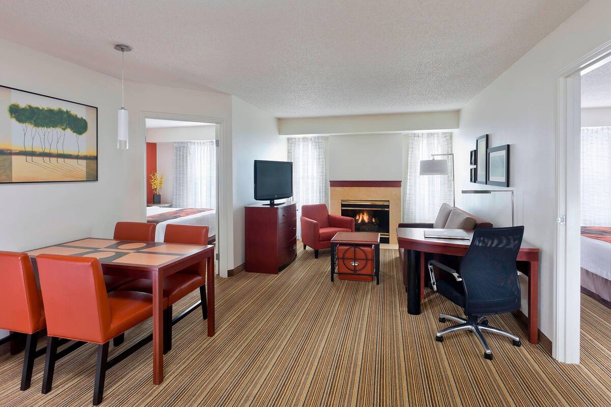A hotel room with a dining area, a TV, a fireplace, and a bed.