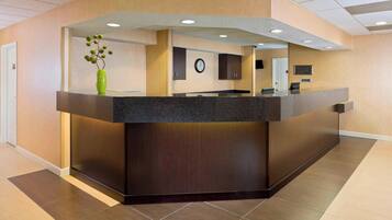 A reception desk with a dark countertop, a green vase with flowers, and a clock on the wall.