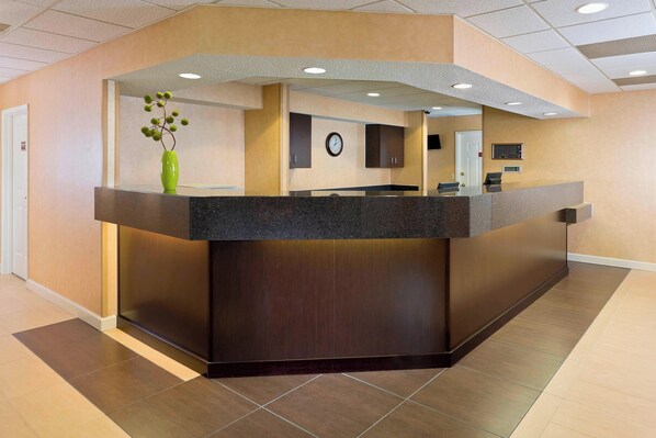 A reception desk with a dark countertop, a green vase with flowers, and a clock on the wall.