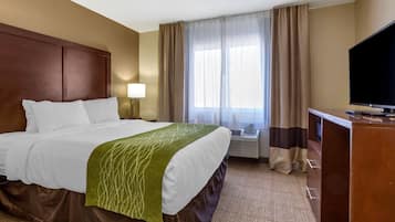 Habitación de hotel con cama, escritorio, televisor y ventana con cortinas.
