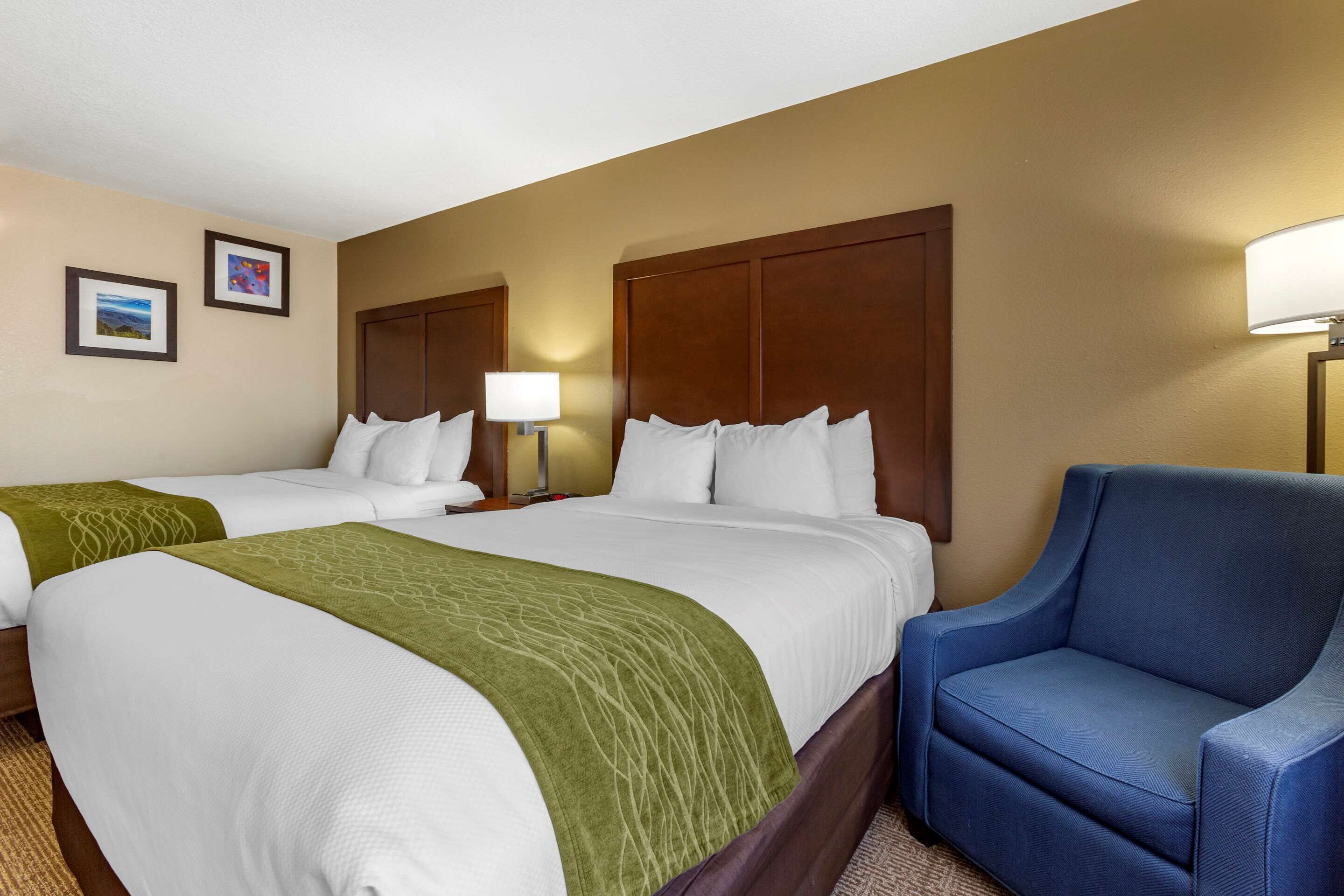 A hotel room with two beds, a blue armchair, and a lamp.