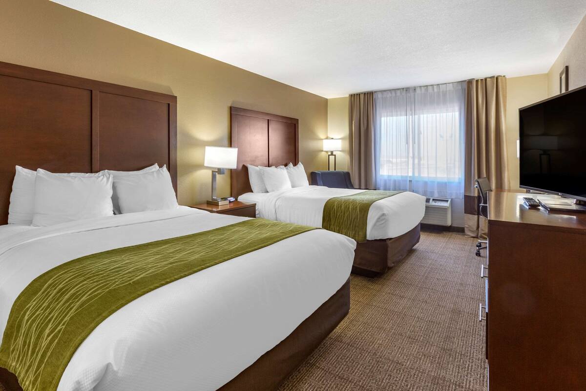 A hotel room with two beds, a flat-screen TV, a desk, and a window with curtains.
