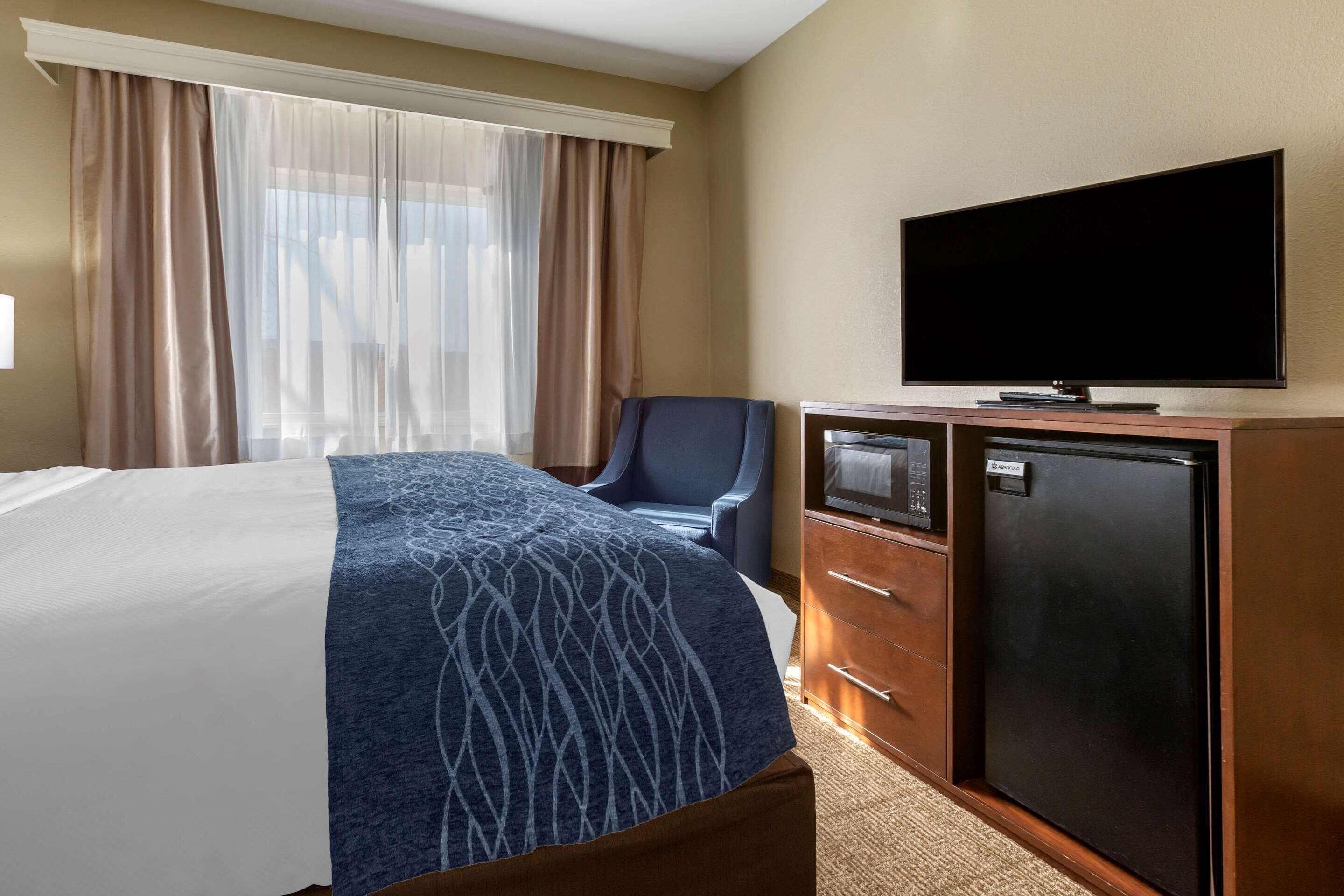 Ein Hotelzimmer mit einem Bett, einem Schreibtisch, einem Fernseher, einem Kühlschrank und einem Sessel.