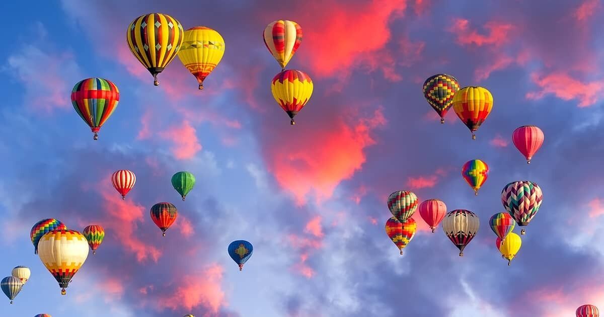 A variety of hot air balloons against a colorful sky.