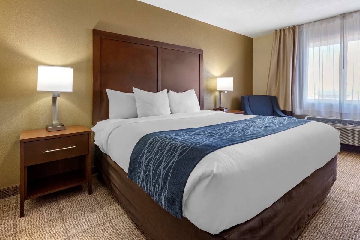A hotel room with a large bed, two bedside tables with lamps, a chair, and a window with curtains.