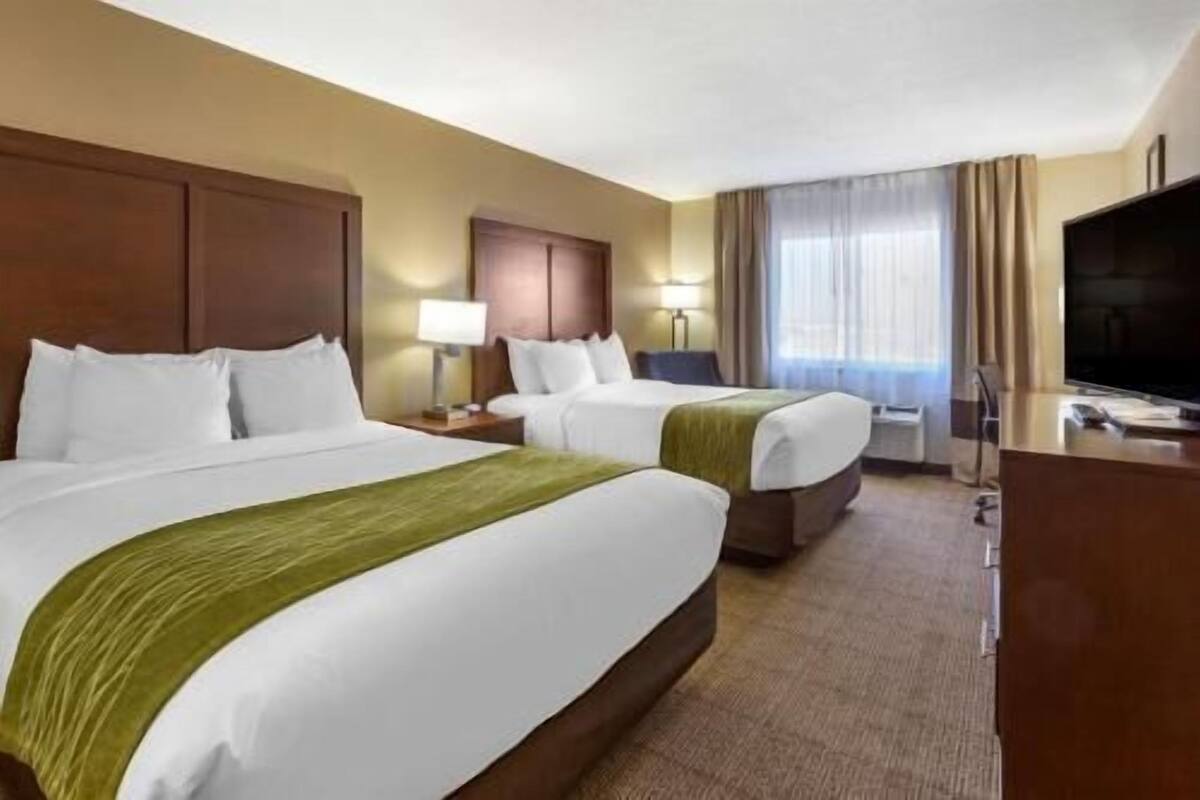 A hotel room with two beds, a desk, a TV, and a window with curtains.
