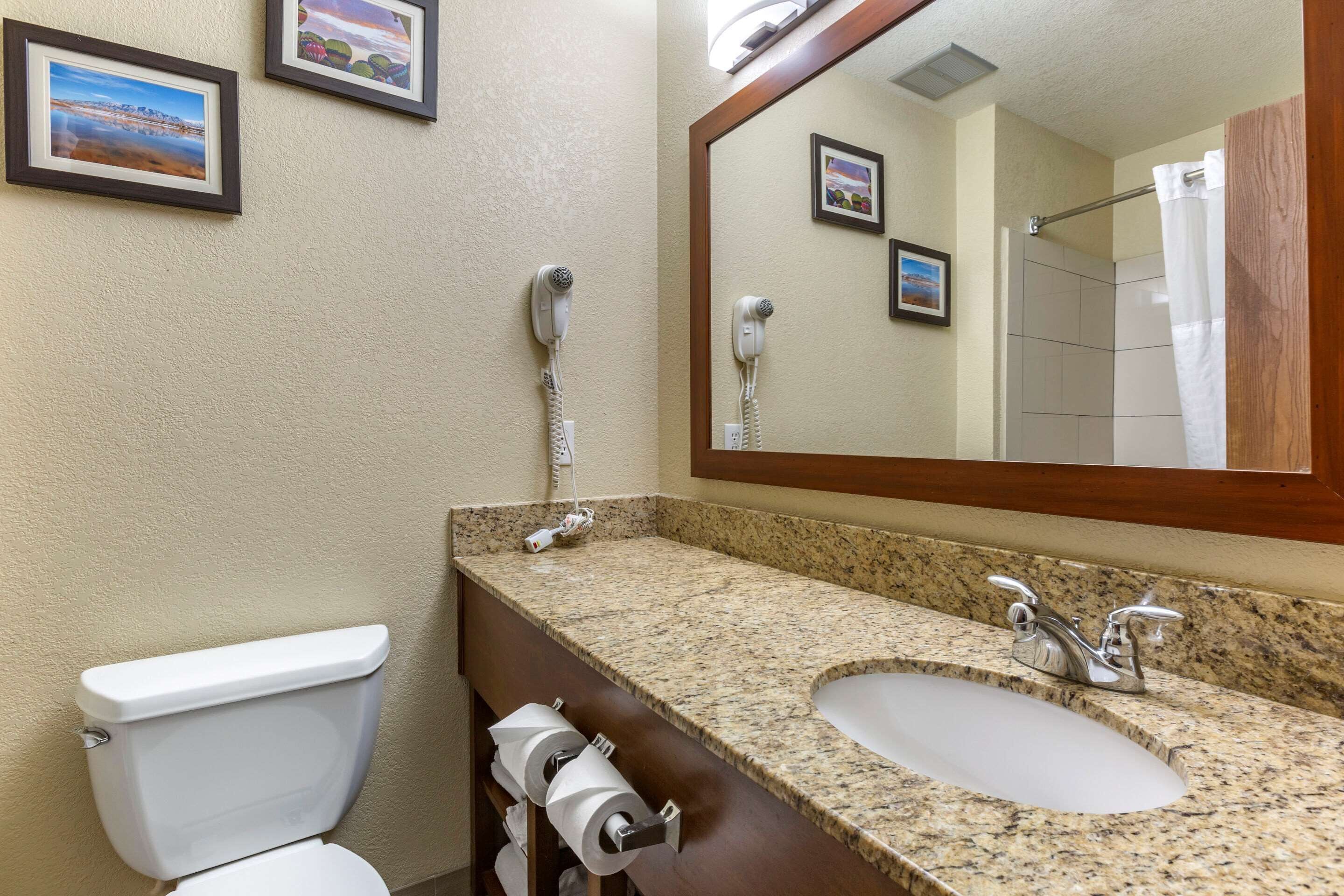 A bathroom with a toilet, sink, and two hair dryers mounted on the wall.