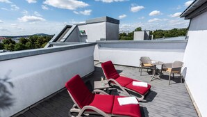 A rooftop terrace with two red lounge chairs, a small table, and a chair. - Arvena Kongress (Bayreuth)