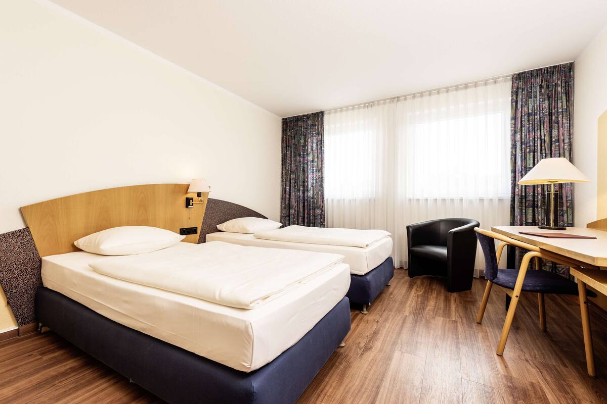 A hotel room with two beds, a desk, and a chair.