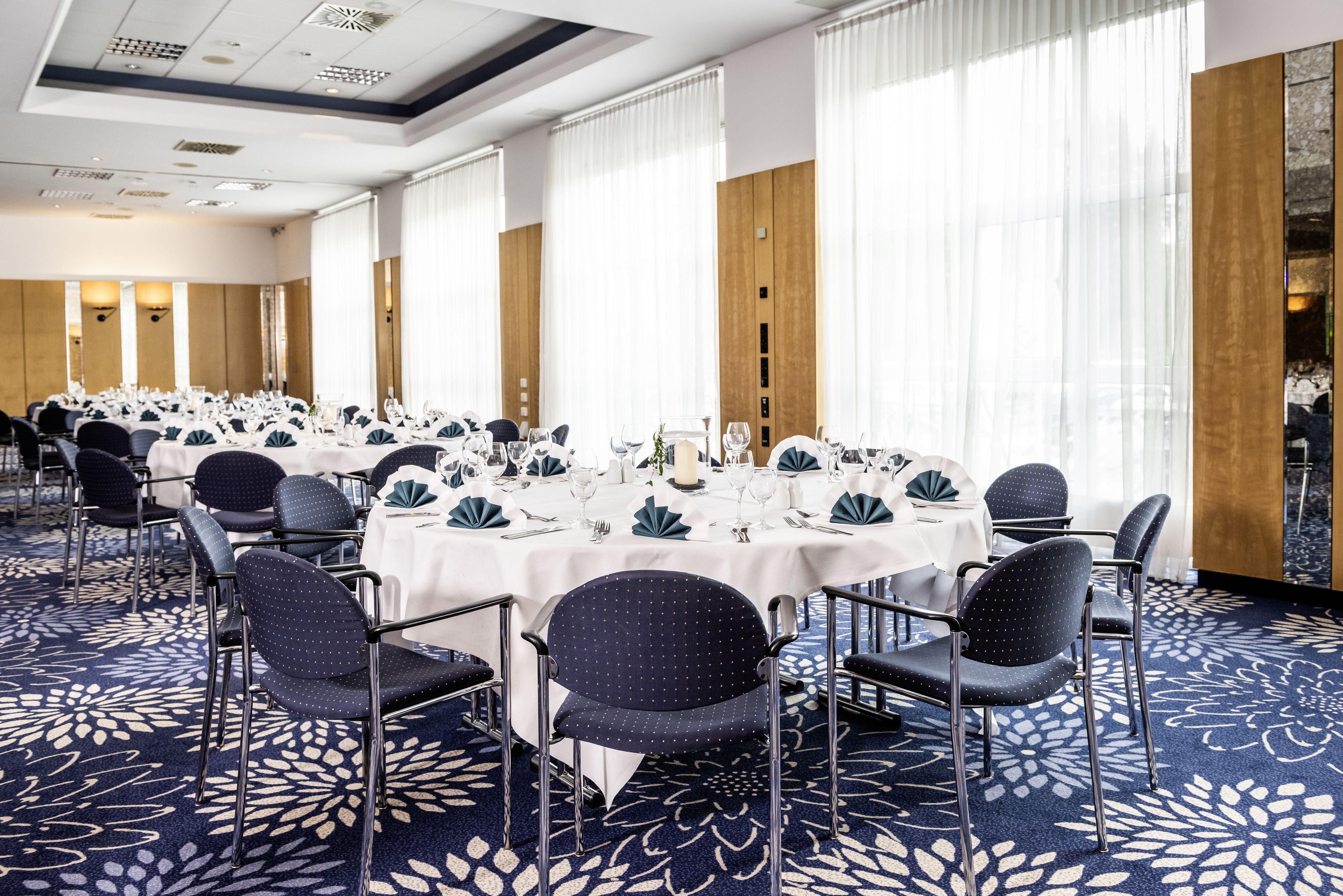 Un salón de conferencias con mesas redondas, sillas y piso alfombrado.
