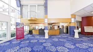A hotel lobby with a blue floral carpet, a reception desk, and a staircase to the upper level. - Arvena Kongress (Bayreuth)
