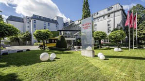 A modern hotel with a clear sky, a well-maintained lawn, and a bus service nearby. - Arvena Kongress (Bayreuth)