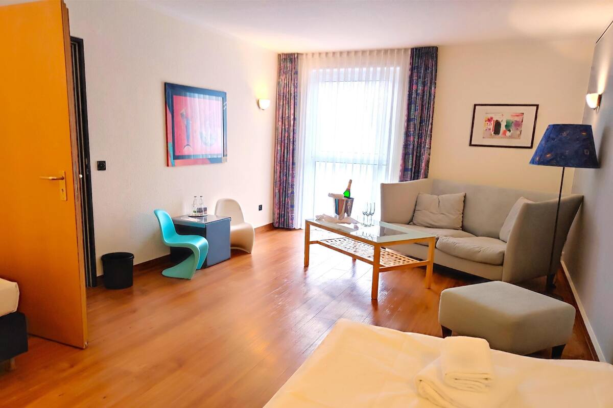 A hotel room with a bed, a sofa, a coffee table, a desk with a chair, and a window with curtains.
