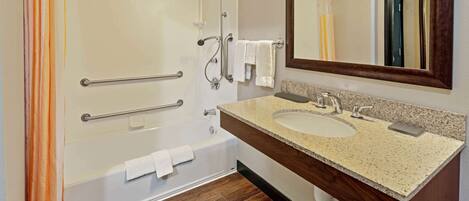 A modern bathroom with a bathtub, two sinks, a large mirror, and wooden flooring.