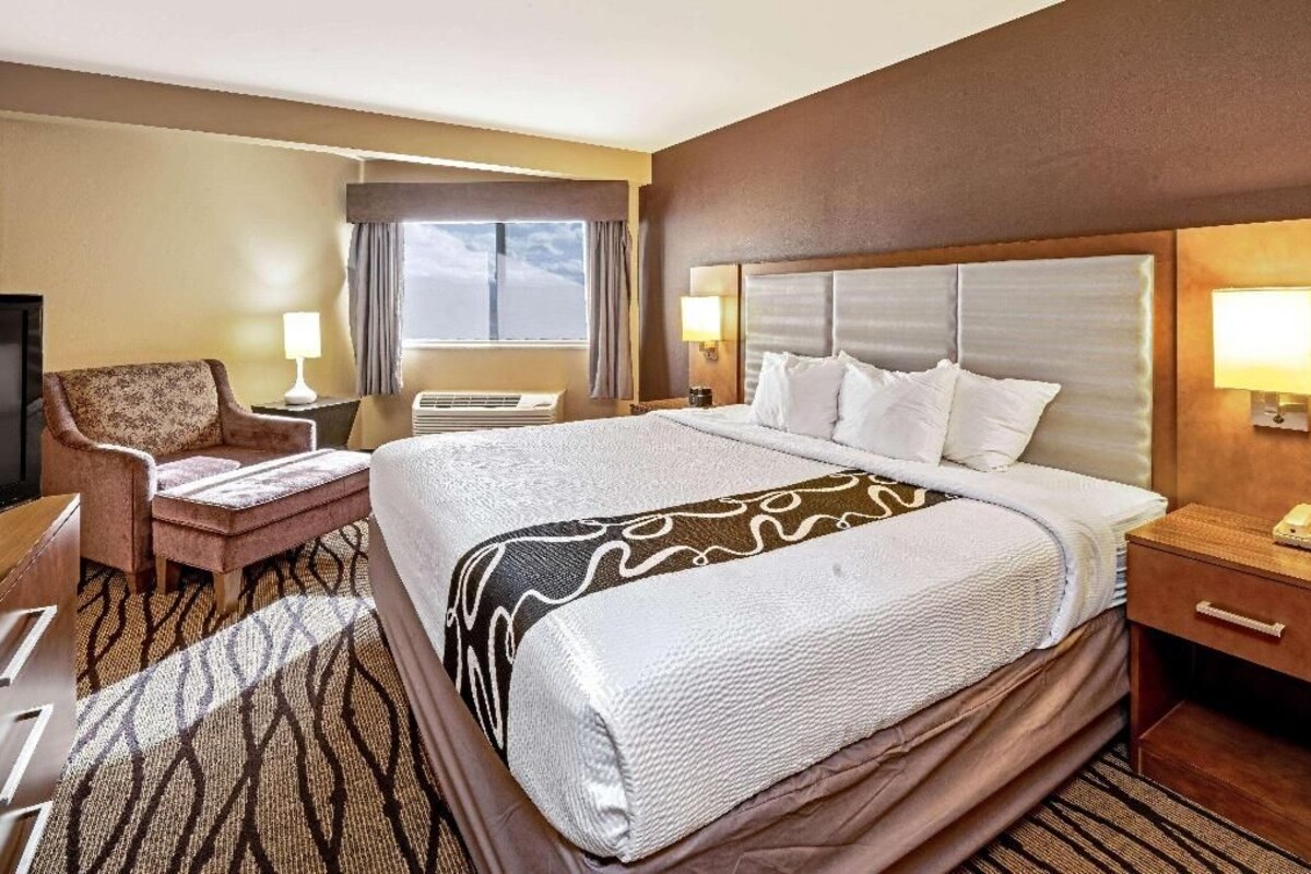 Ein Hotelzimmer mit einem großen Bett, einem Sessel, einem Schreibtisch, einer Lampe und einem Fenster.