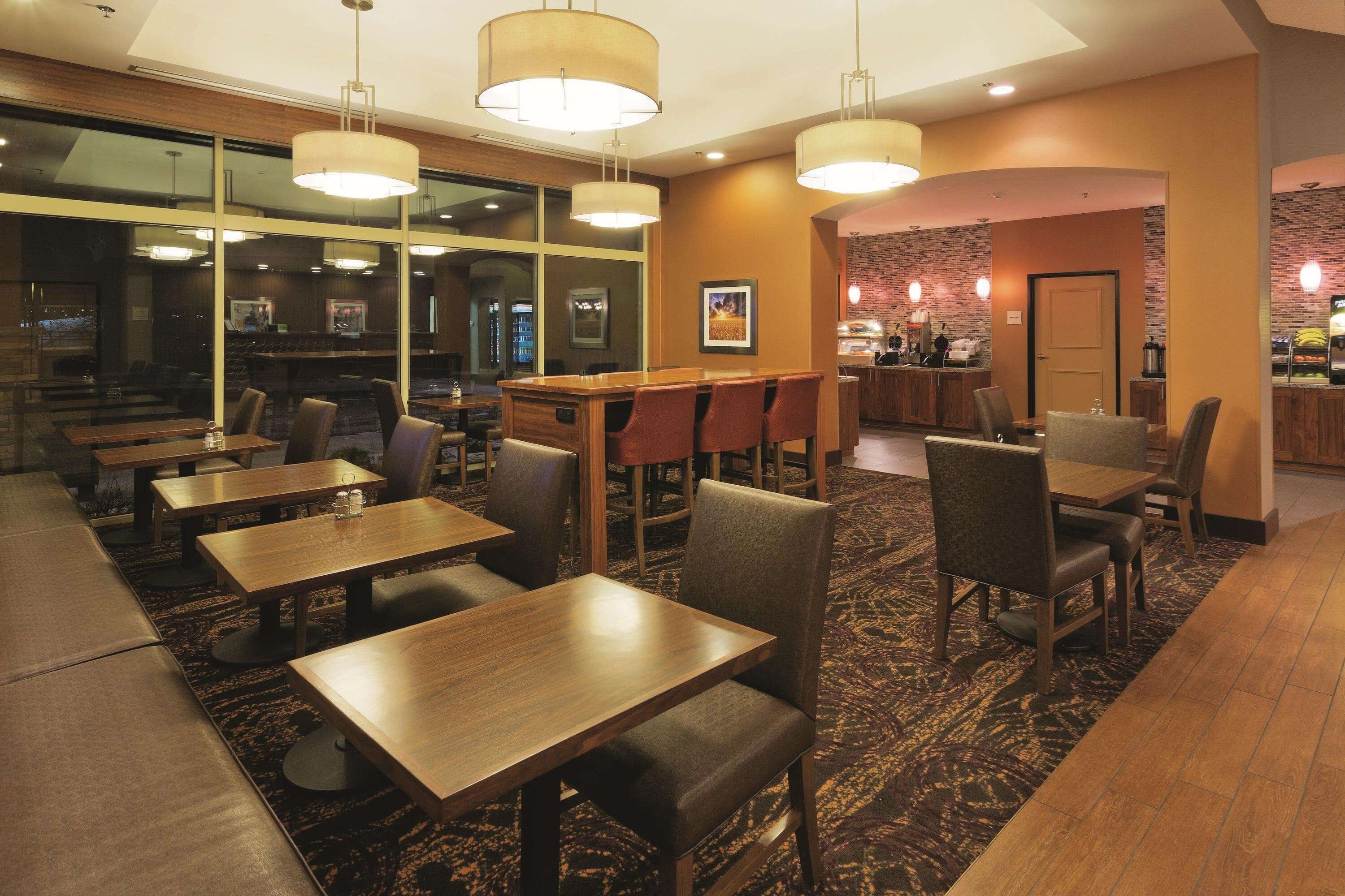 A restaurant with multiple tables and chairs, a bar area, and a view through large windows.