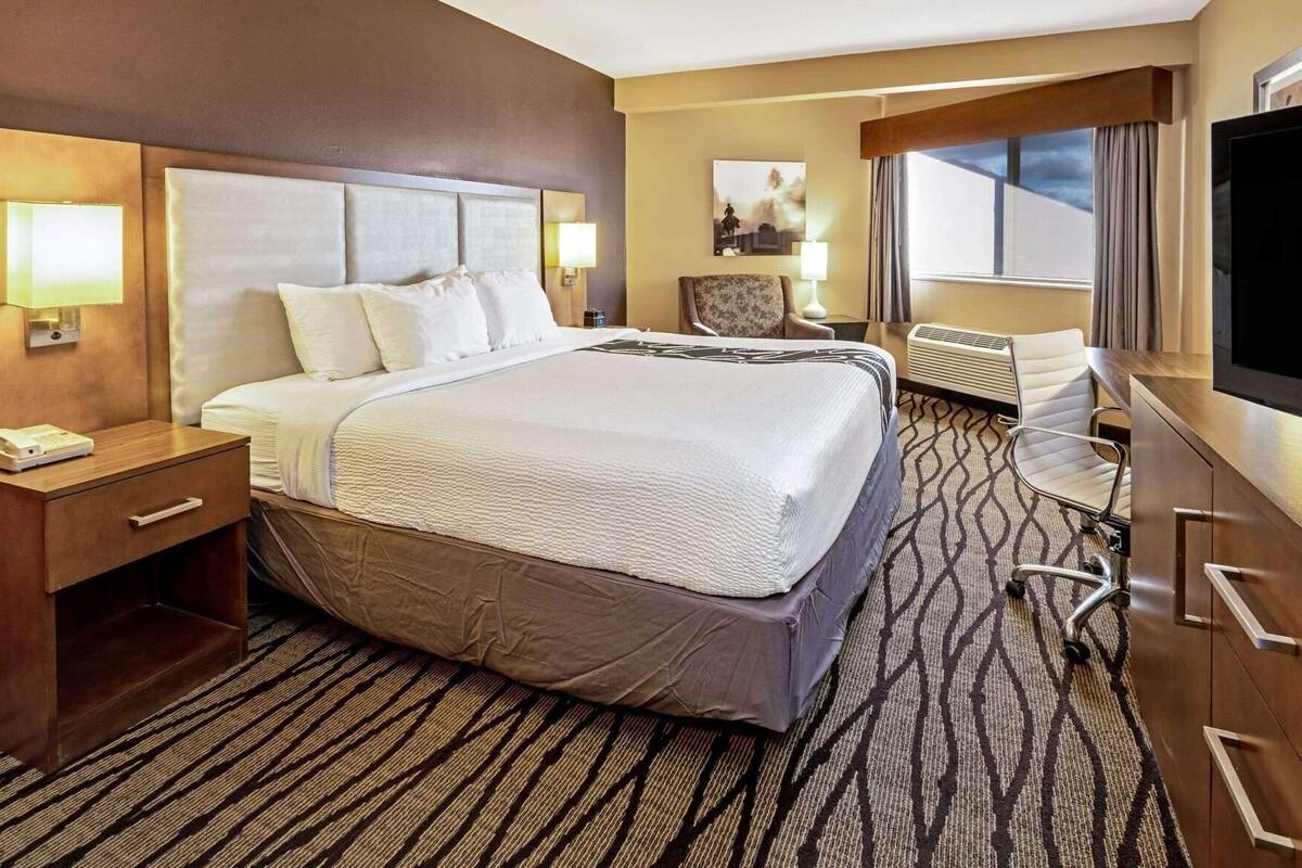 A hotel room with a large bed, a desk, a chair, a TV, and a window with curtains.