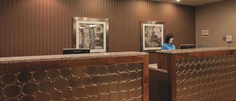 A reception desk with a wooden panel design, framed artwork on the wall, and a sign indicating manager on duty.