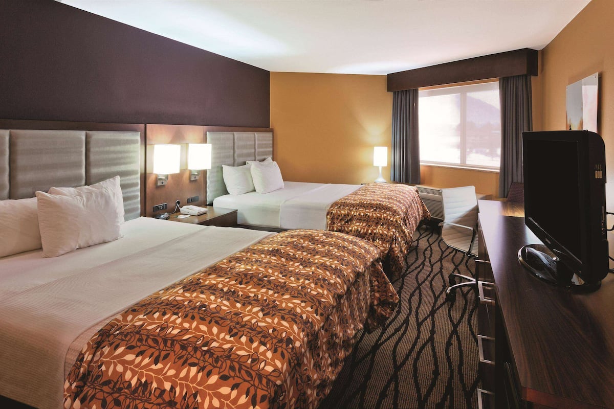 A hotel room with two beds, a desk, a television, and a large window with curtains.