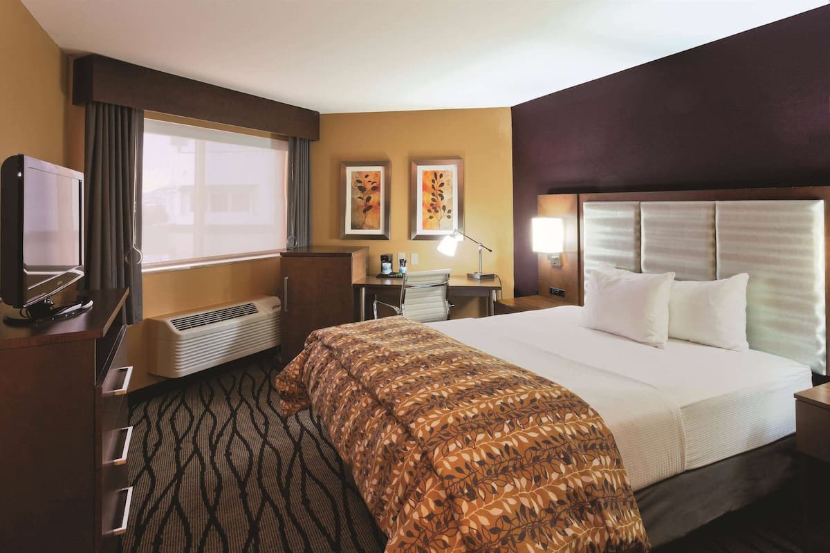 A hotel room with a large bed, a desk with a chair, a television, and two framed pictures on the wall.