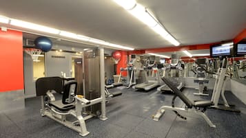 A gym with various exercise equipment, a basketball hoop, and a television screen.