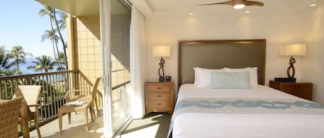 A hotel room with a balcony, a bed with a headboard, two bedside tables with lamps, and a ceiling fan.