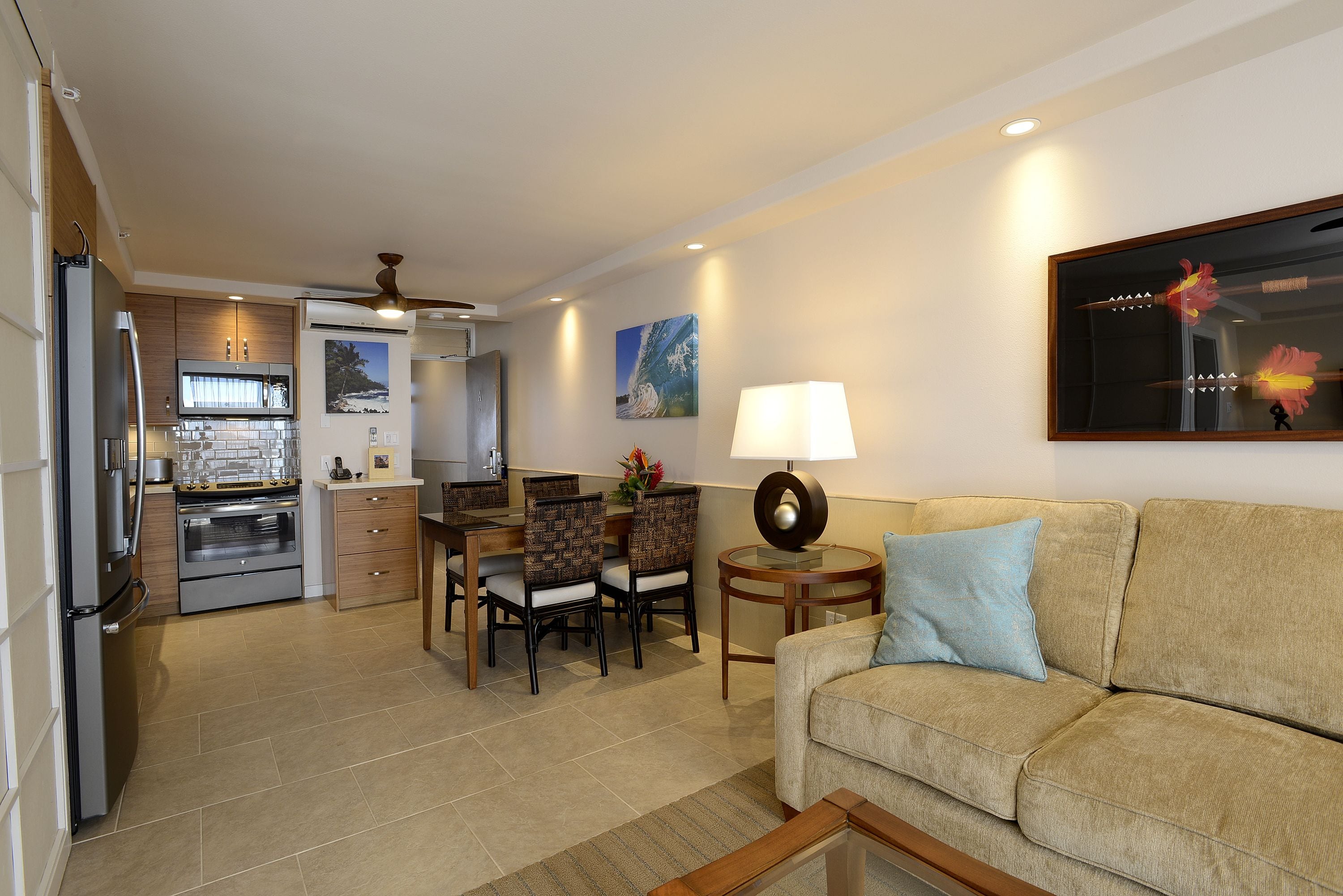 A modern kitchen with built-in appliances, a dining area with chairs, a sofa, and a lamp.