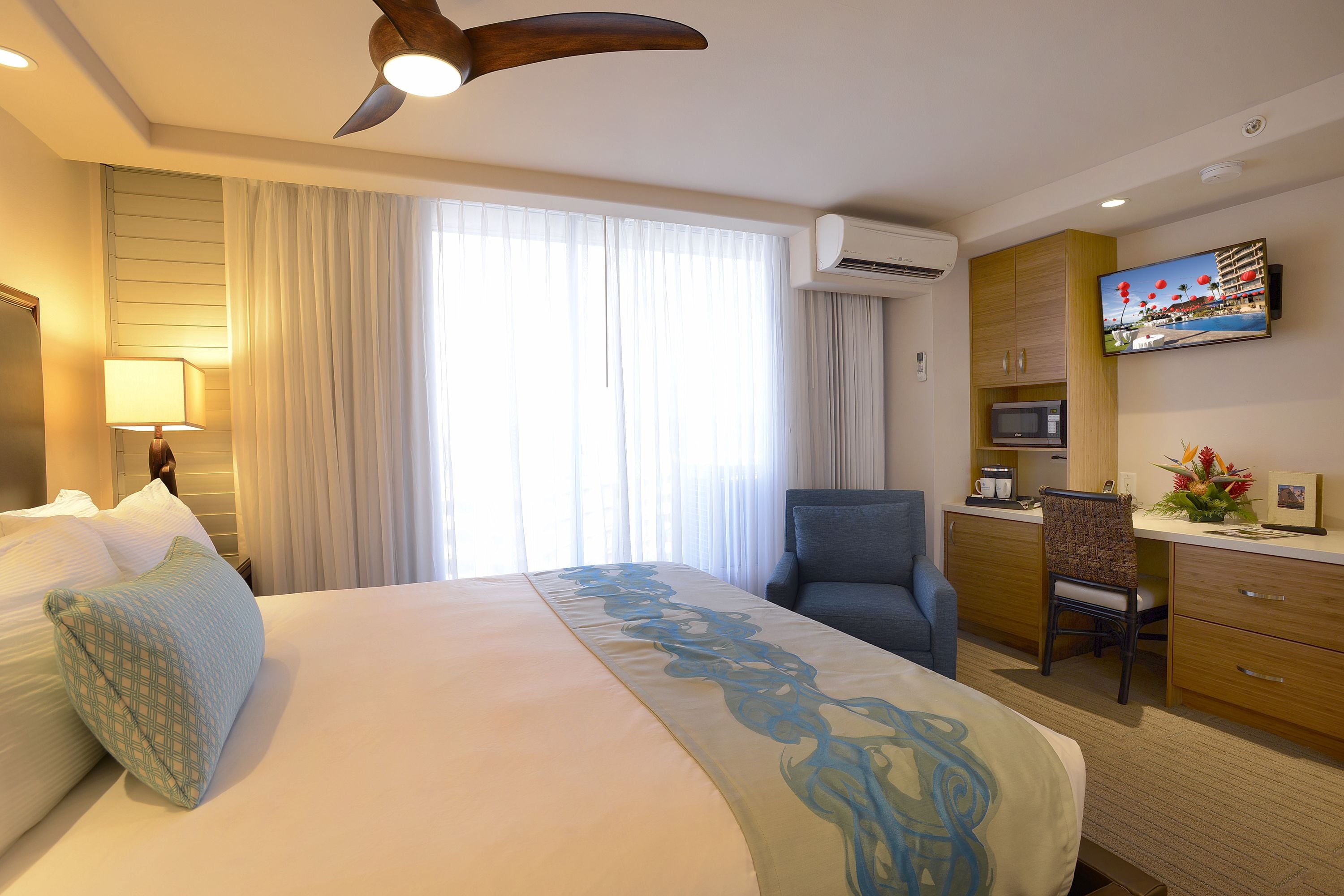 A hotel room with a bed, a desk, a chair, an air conditioning unit, and a television.