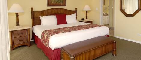 A neatly arranged bedroom with a large bed, two bedside tables, a bench, a ceiling fan, a painting, and a mirror.