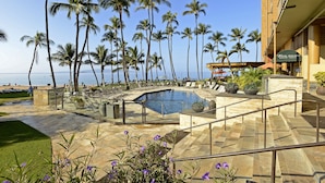 Zona de piscina con palmeras, vista a la playa y un edificio con un letrero que dice "Five Palms Beach Grill".