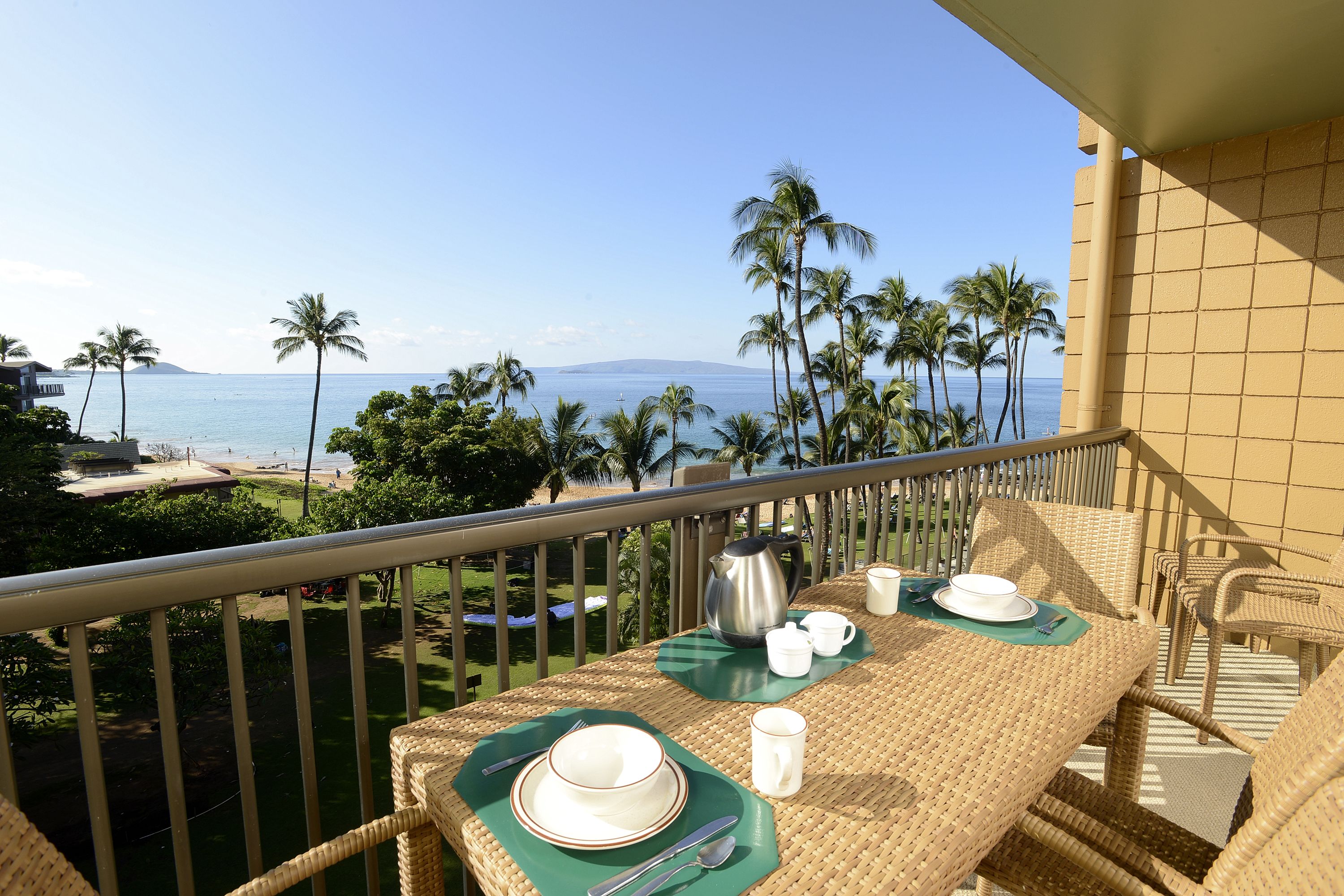 A balcony with a table set for breakfast overlooking a beach with palm trees and the ocean.