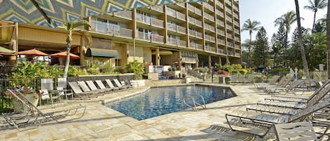 Un área de piscina de hotel con sillones de descanso, una piscina y un edificio de varios pisos con balcones.