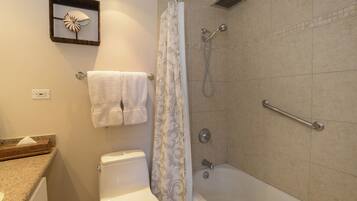 A bathroom with a toilet, a shower with a grab bar, a towel rack, and a decorative wall piece.
