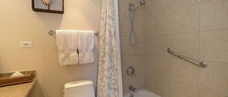 A bathroom with a toilet, a shower with a grab bar, a towel rack, and a decorative wall piece.