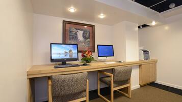 A workspace with two computers, a desk, two patterned chairs, a framed picture, and a printer.
