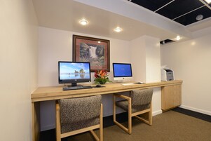 A workspace with two computers, a desk, two patterned chairs, a framed picture, and a printer.