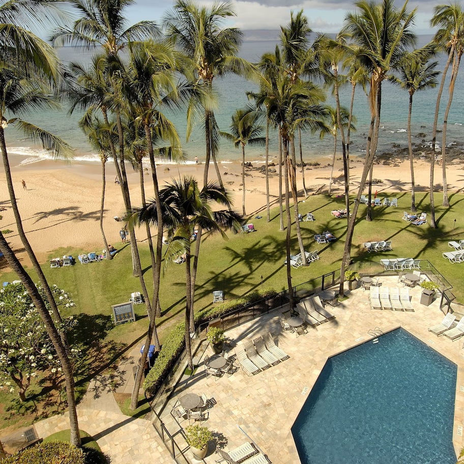 A resort with a pool, lounge chairs, and palm trees.