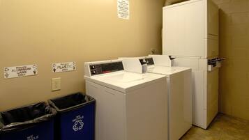 A laundry area with two washing machines, a dryer, recycling bins, and a sign indicating recycling instructions.