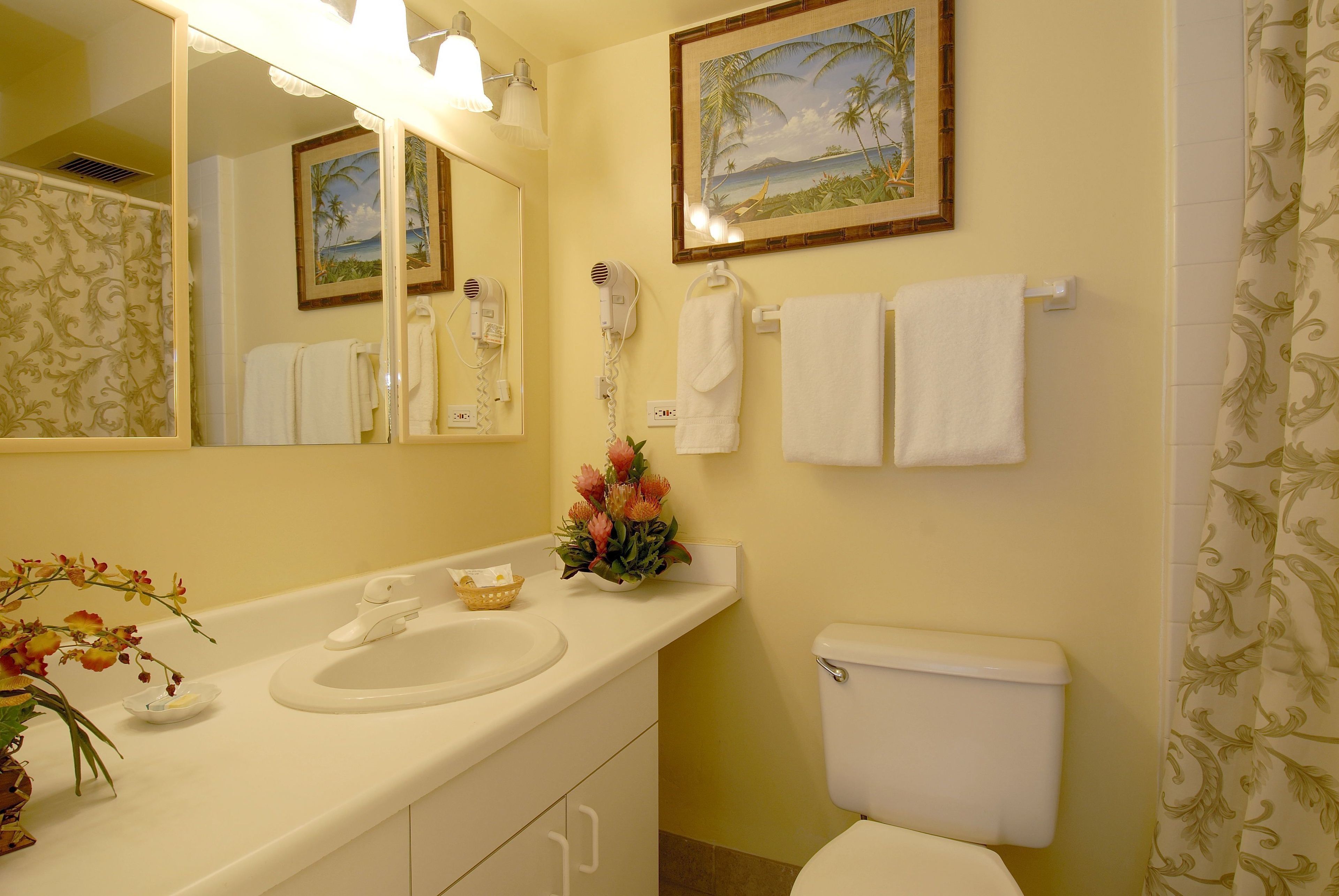 A bathroom with a sink, mirror, and toilet. There are towels hanging on the wall and a shower curtain.