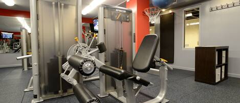 Une salle de sport équipée de divers appareils d’exercice, d’un panier de basket et d’un miroir au mur.