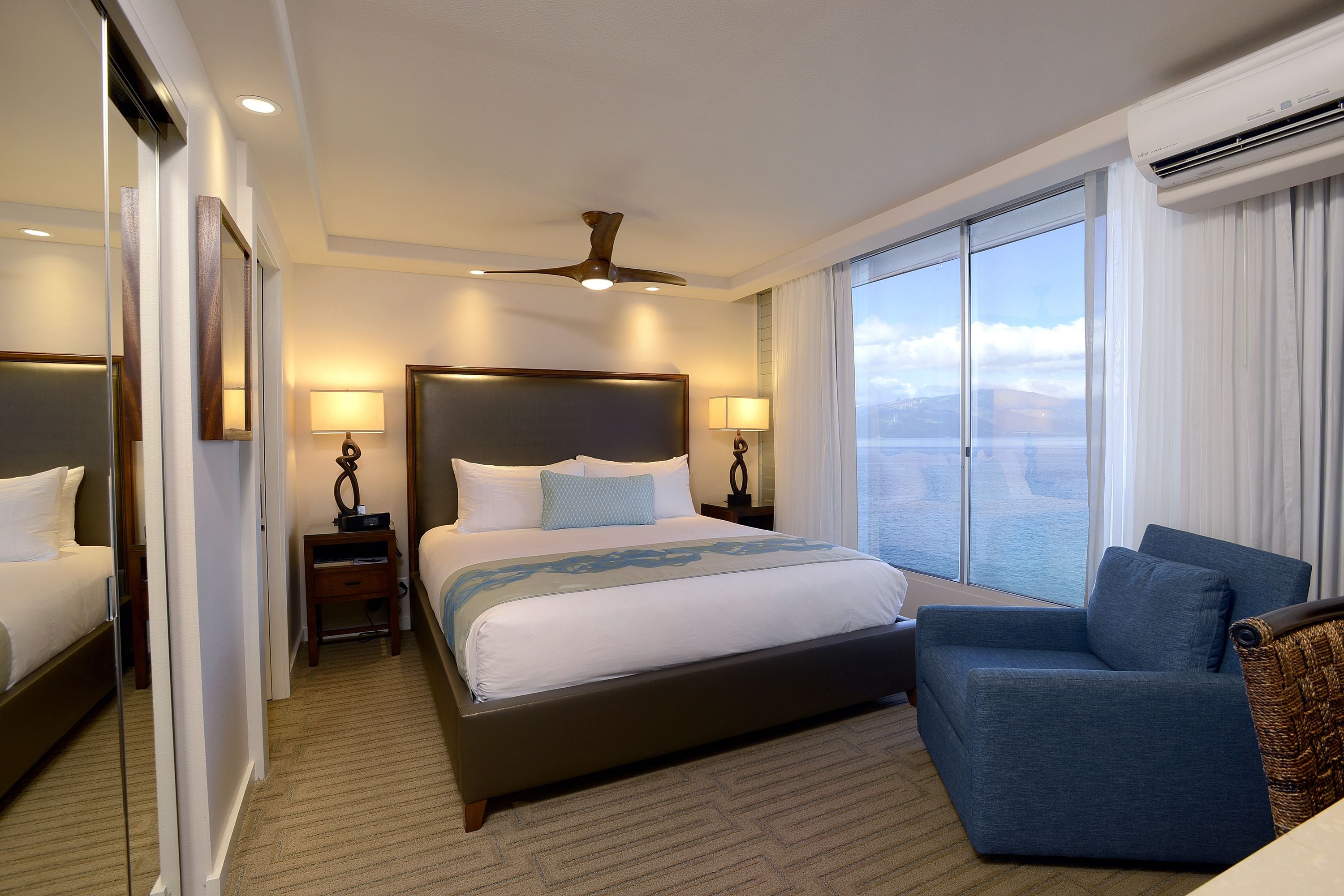 A hotel room with a large bed, a sofa, a ceiling fan, and a view of the outdoors.