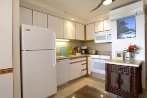 A modern kitchen with white appliances, wooden cabinets, and a view of the beach through the window.